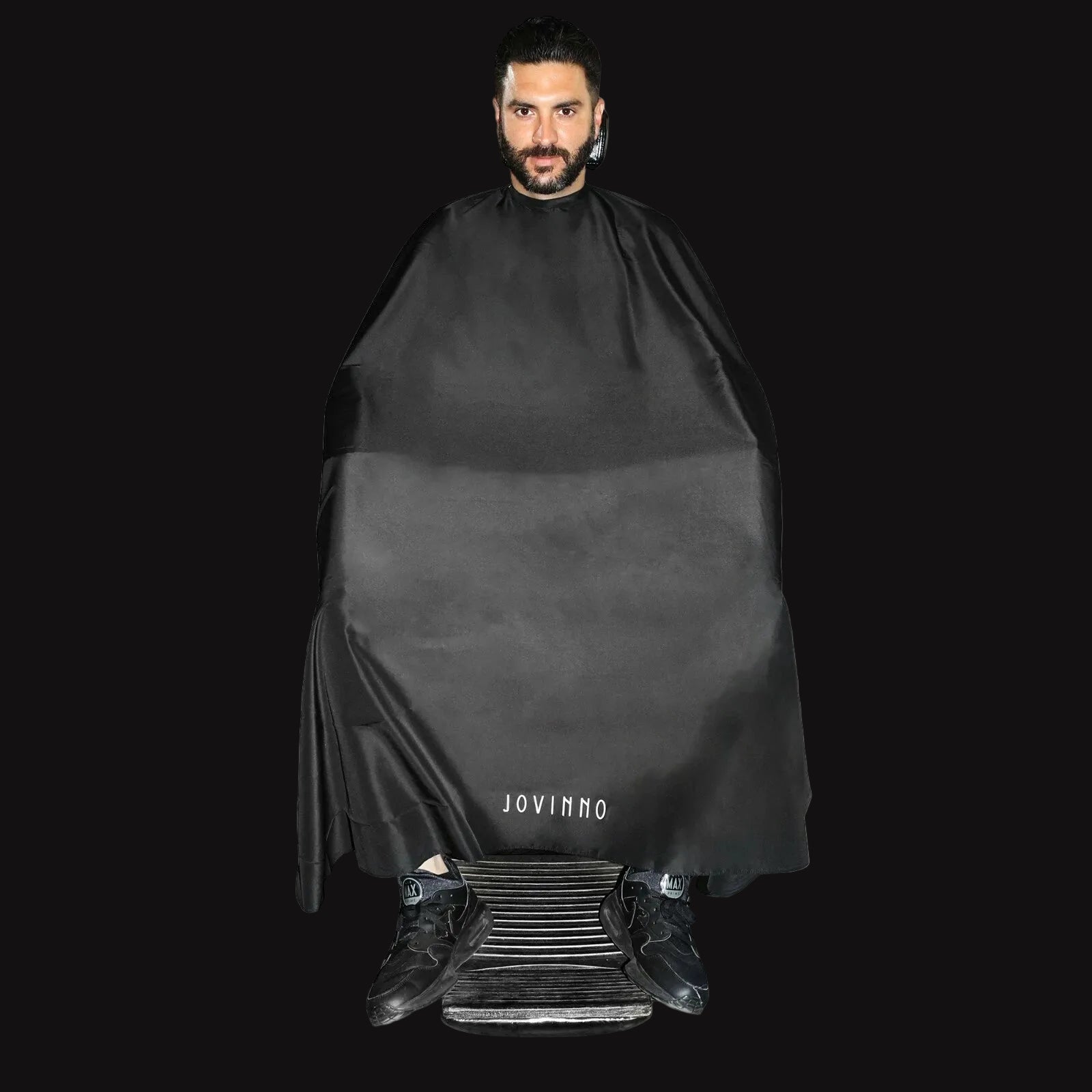 Man wearing a black barber cape with 'JOVINNO' branding on a white background